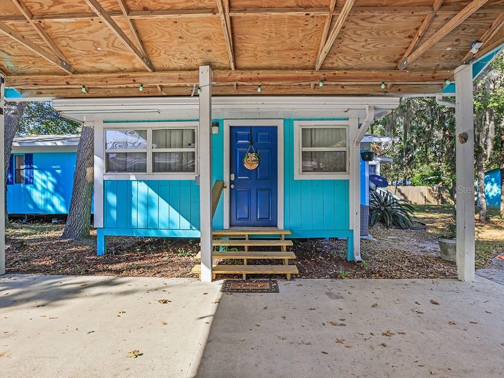 A bright blue house with a dark blue front door sits under a wooden carport — 112 8TH STREET NE, STEINHATCHEE, FL