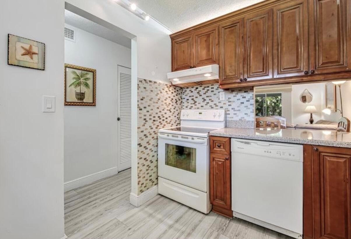 A kitchen features wood cabinets, white appliances, and a mosaic tile backsplash — 2855 Garden Drive S # 102, FL 33461, FL
