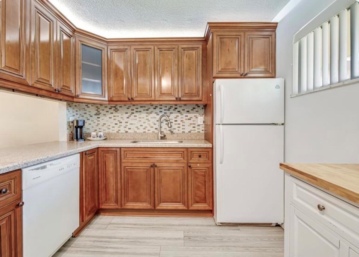 A kitchen featuring wood cabinets, a mosaic tile backsplash, granite countertops, and white appliances — 2855 Garden Drive S # 102, FL 33461, FL