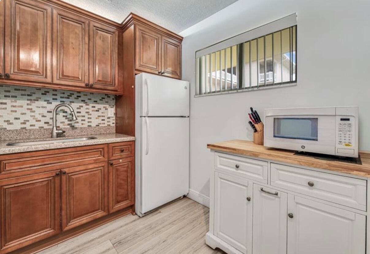 A kitchen features wood cabinets, a white refrigerator, a microwave on a white cabinet, and backsplash — 2855 Garden Drive S # 102, FL 33461, FL
