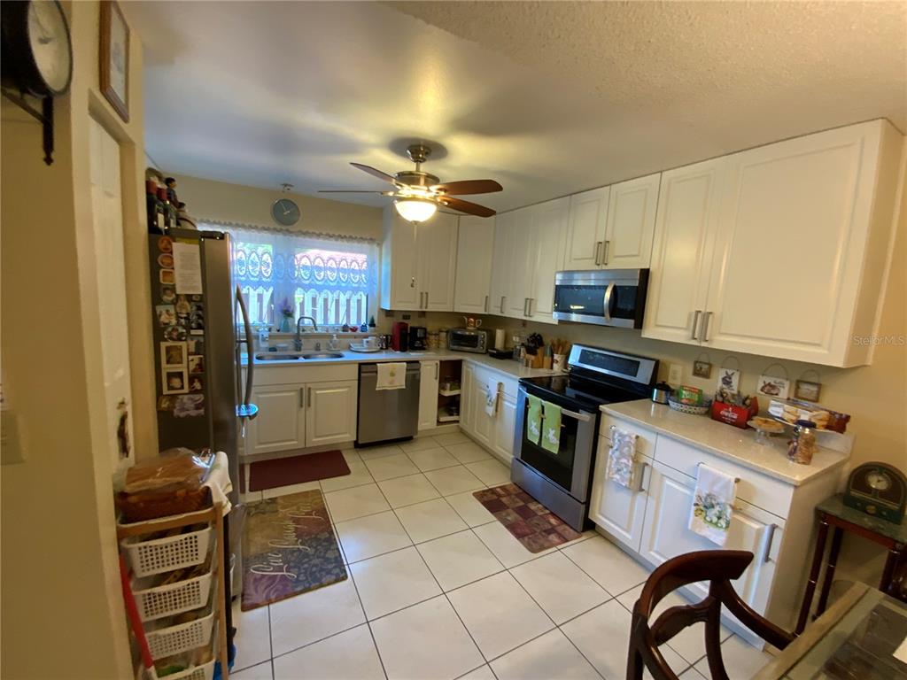 A kitchen features white cabinetry, stainless steel appliances, a ceiling fan, and tiled flooring — 517 HUNTER CIRCLE, KISSIMMEE, FL