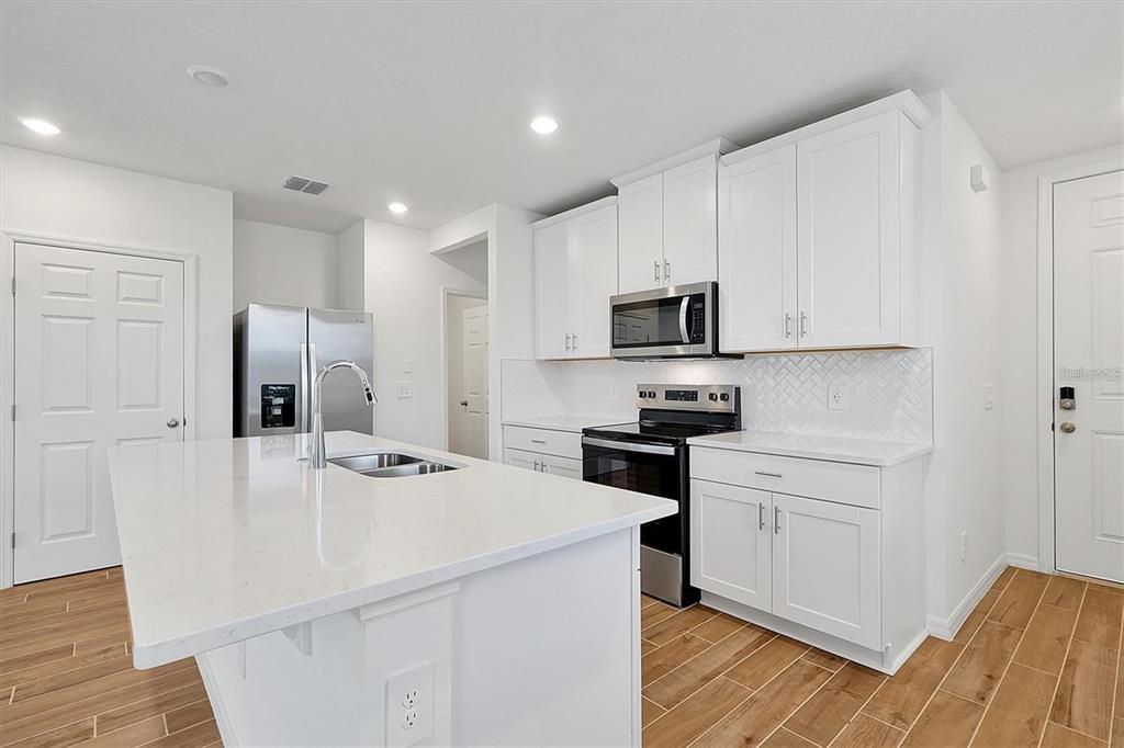 A modern kitchen features white cabinetry, a large center island, and stainless steel appliances — 4330 RESTFUL FALLOW COVE, ST CLOUD, FL