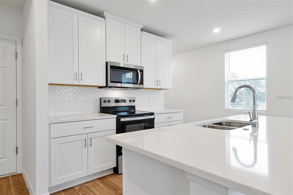 A modern kitchen features white cabinets, stainless steel appliances, and a white quartz island countertop — 4330 RESTFUL FALLOW COVE, ST CLOUD, FL