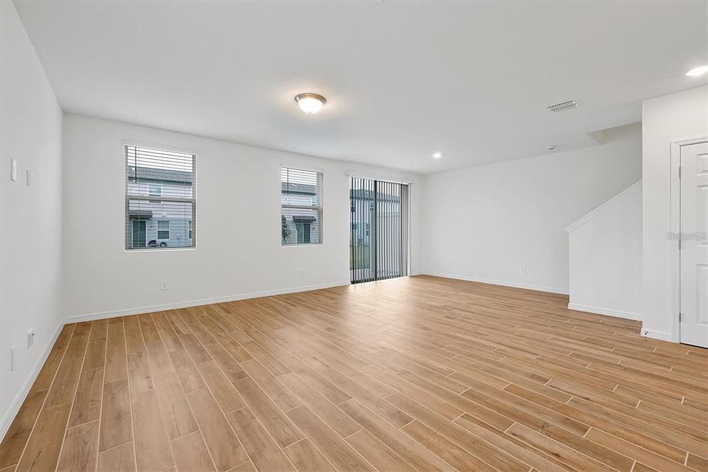 An empty living room features light wood-look tile flooring, white walls, and sliding glass doors — 4330 RESTFUL FALLOW COVE, ST CLOUD, FL