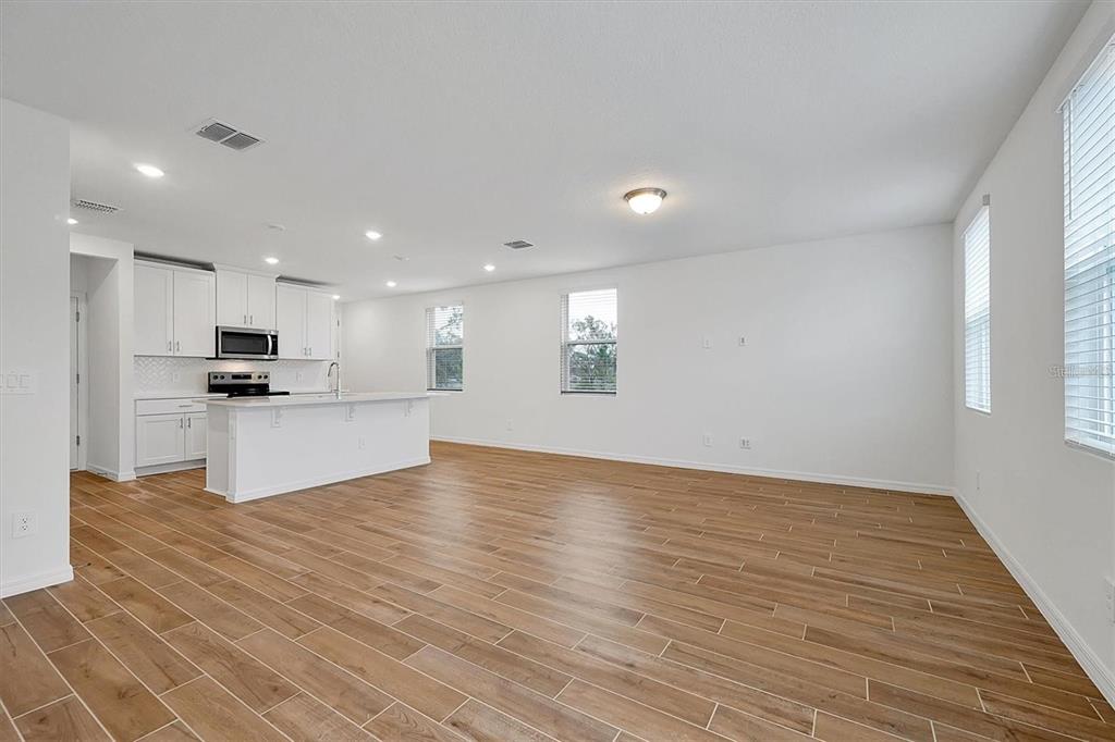 An open-concept kitchen and living area features white cabinets, a center island, and wood-look flooring — 4330 RESTFUL FALLOW COVE, ST CLOUD, FL