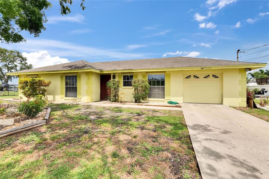 A single-story yellow house with a concrete driveway and a front lawn under a blue sky — 814 SEABREEZE DRIVE, RUSKIN, FL