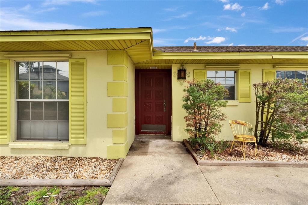 A yellow house exterior features a red front door, shutters, and a concrete walkway — 814 SEABREEZE DRIVE, RUSKIN, FL
