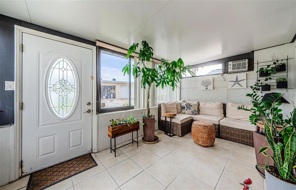 A sunroom features tile flooring, wicker furniture, a large potted plant, and a white door — 2739 SHERBROOKE LANE UNIT B, PALM HARBOR, FL