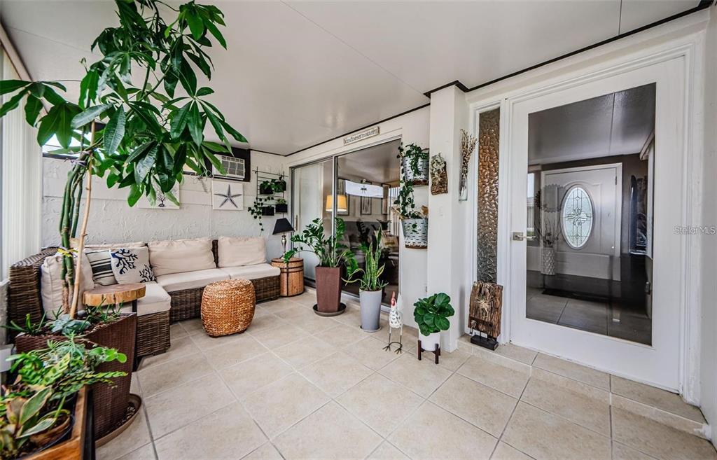 A sunroom features tile flooring, wicker furniture, numerous potted plants, and a glass-paneled entry door — 2739 SHERBROOKE LANE UNIT B, PALM HARBOR, FL