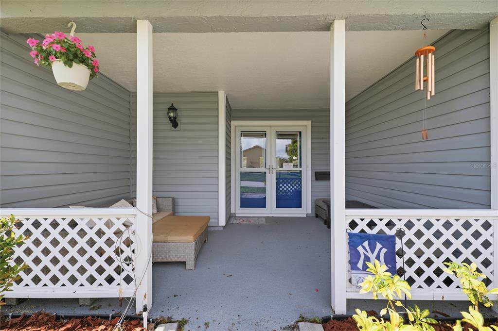 A covered front porch features gray siding, a white lattice railing, and a double glass door — 9342 CAPE CHARLES AVENUE, NEW PORT RICHEY, FL