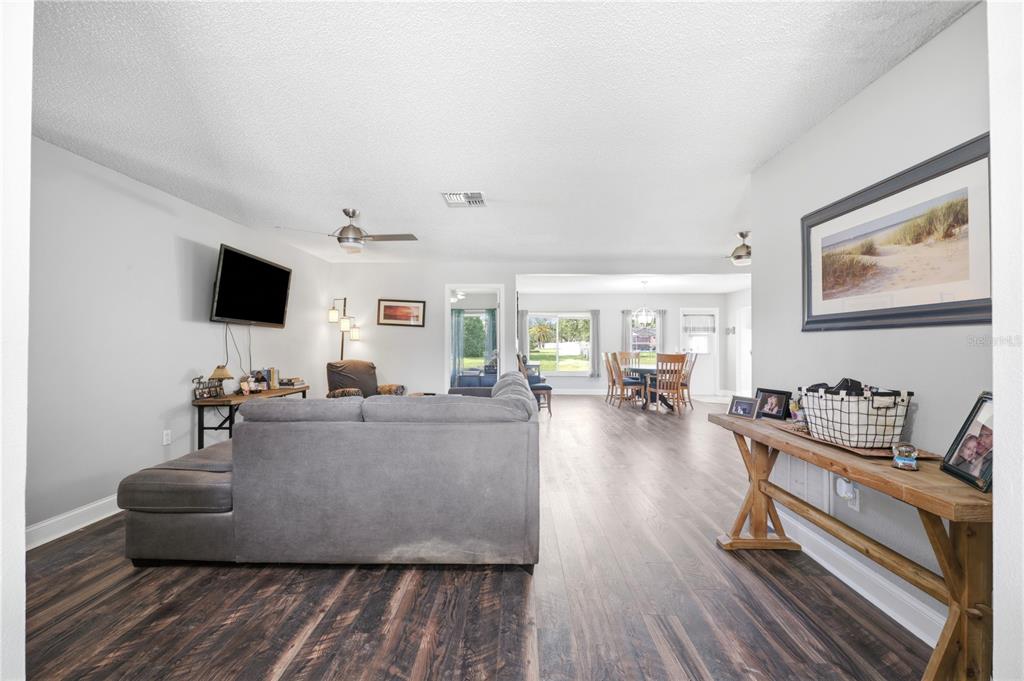 A living room with wood-look flooring, a gray sectional sofa, and an open dining area — 9342 CAPE CHARLES AVENUE, NEW PORT RICHEY, FL