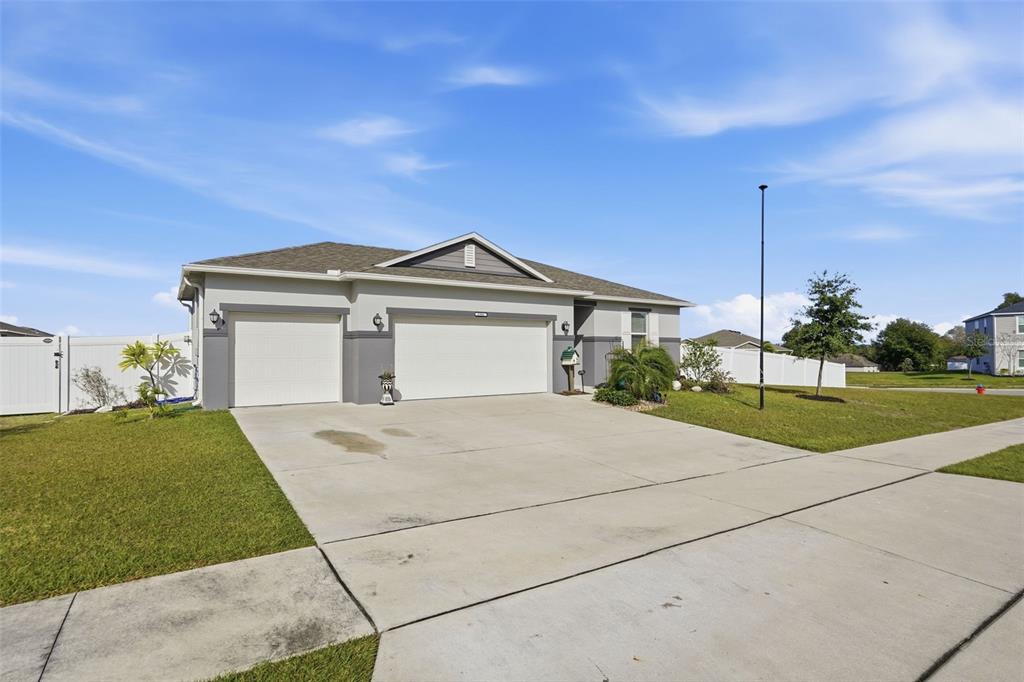 A single-story house with a three-car garage and a concrete driveway under a blue sky — 2201 GLADIOLUS LN LANE, MASCOTTE, FL