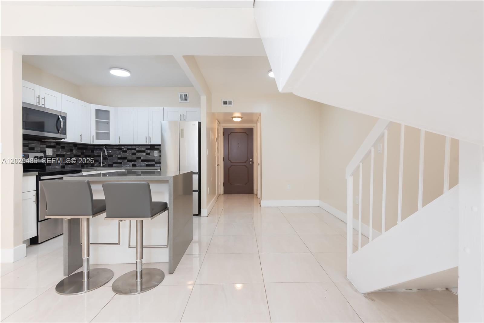 A kitchen with white cabinets and a gray island sits next to a staircase — 300 NW 42nd Ave # 411, Miami FL 33126, MIAMI, FL