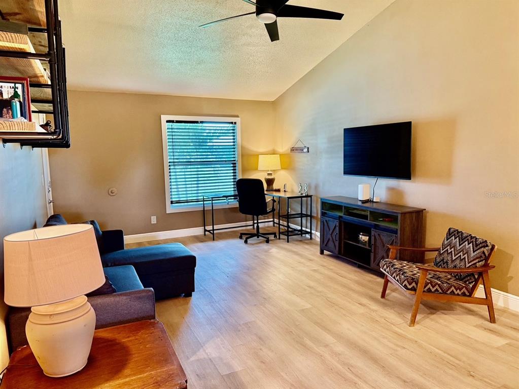 A living room features light wood-look flooring, a dark sofa, a desk, and a television — 11248 PENDLETON AVENUE UNIT A&B, ENGLEWOOD, FL