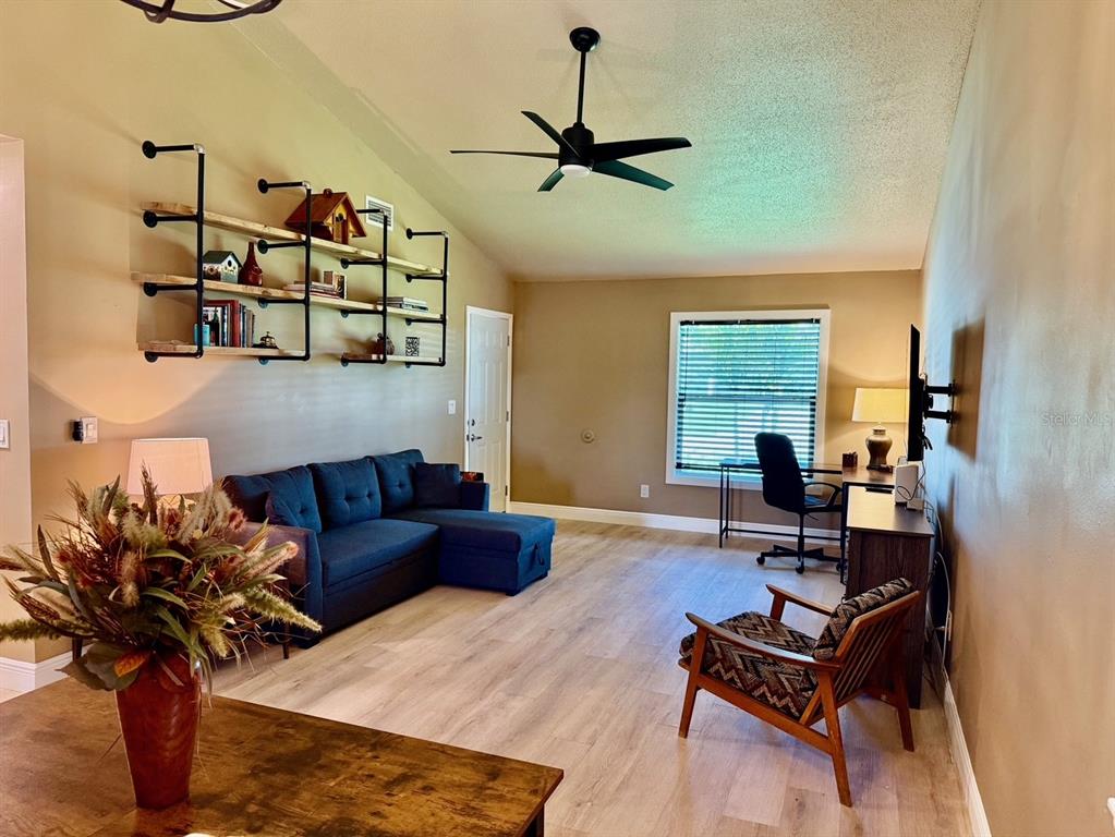 A living room features a blue sectional sofa, industrial-style wall shelving, and light wood flooring — 11248 PENDLETON AVENUE UNIT A&B, ENGLEWOOD, FL
