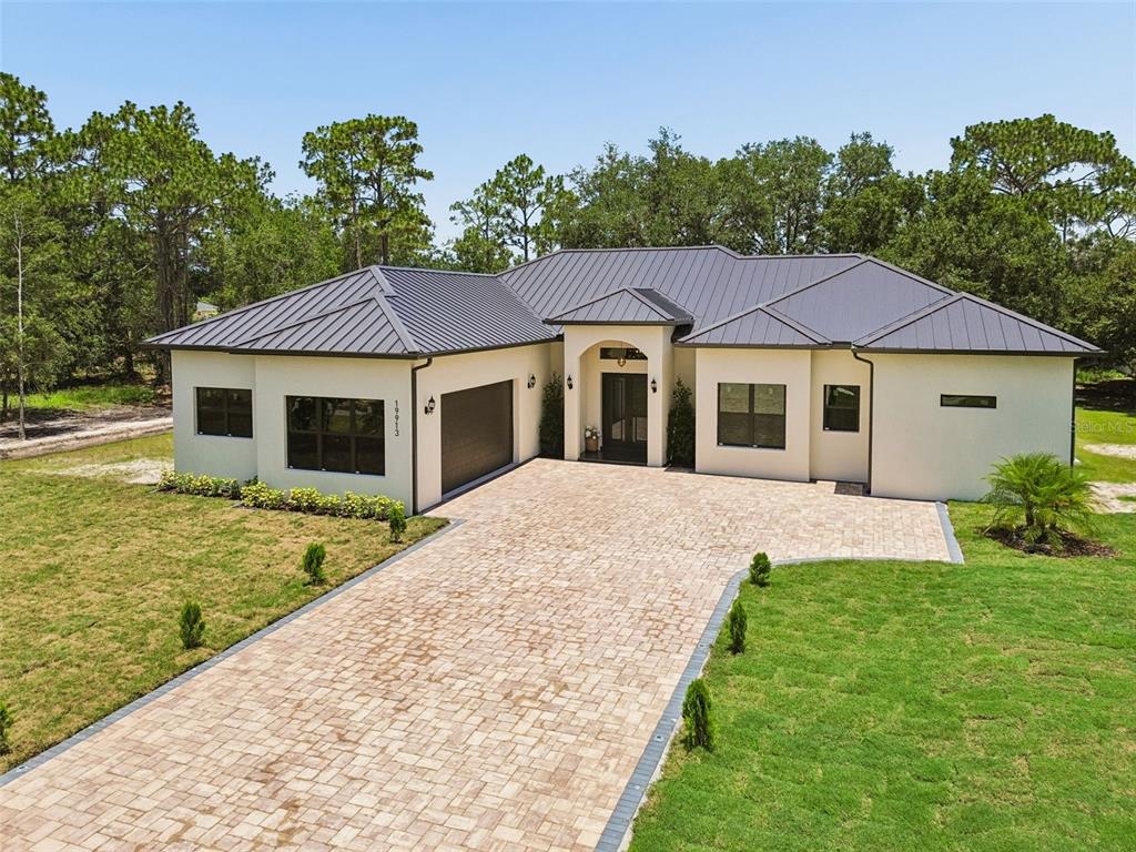 A single-story house with a metal roof, stucco exterior, and a paved driveway — 19913 MOORGATE STREET, ORLANDO, FL