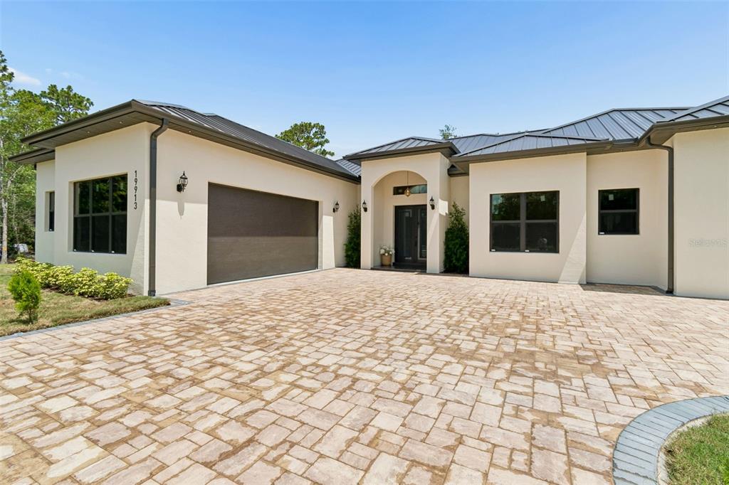 A modern single-story house with a paved driveway, dark garage door, and metal roof — 19913 MOORGATE STREET, ORLANDO, FL