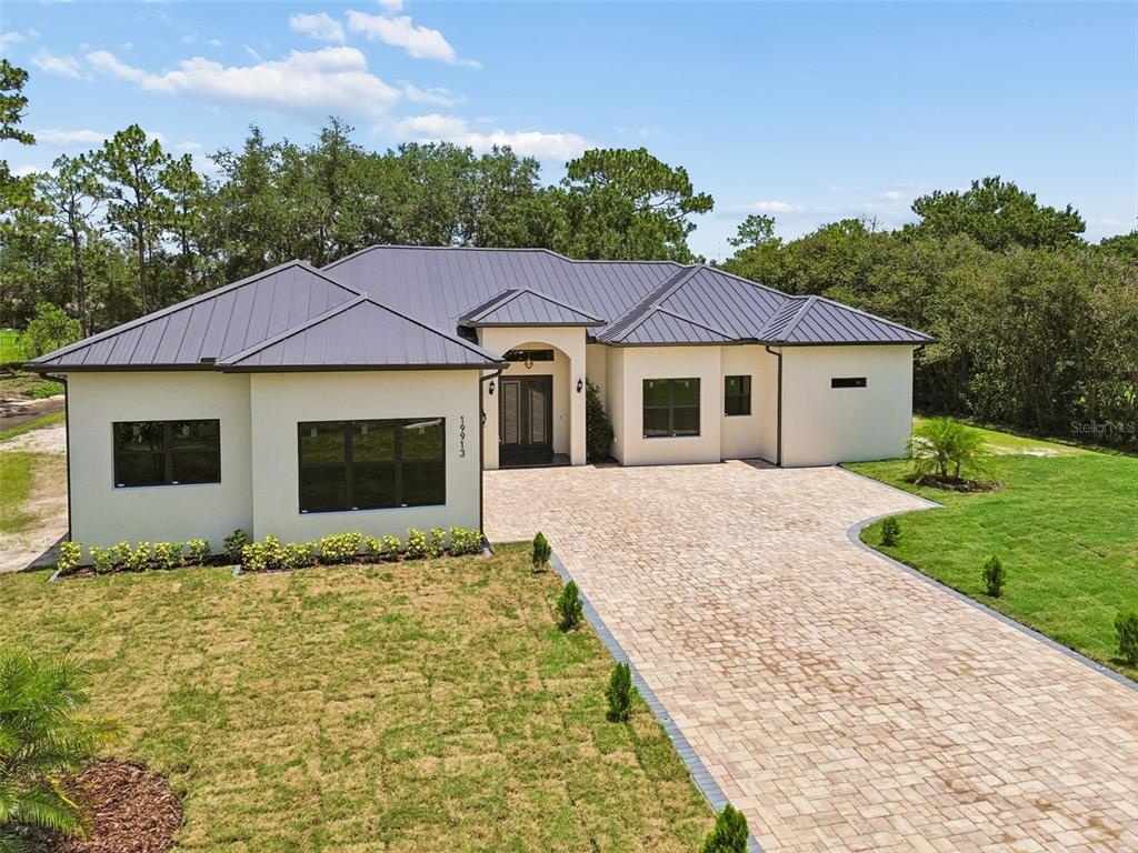 A single-story house with a dark metal roof, stucco exterior, and a paved driveway — 19913 MOORGATE STREET, ORLANDO, FL