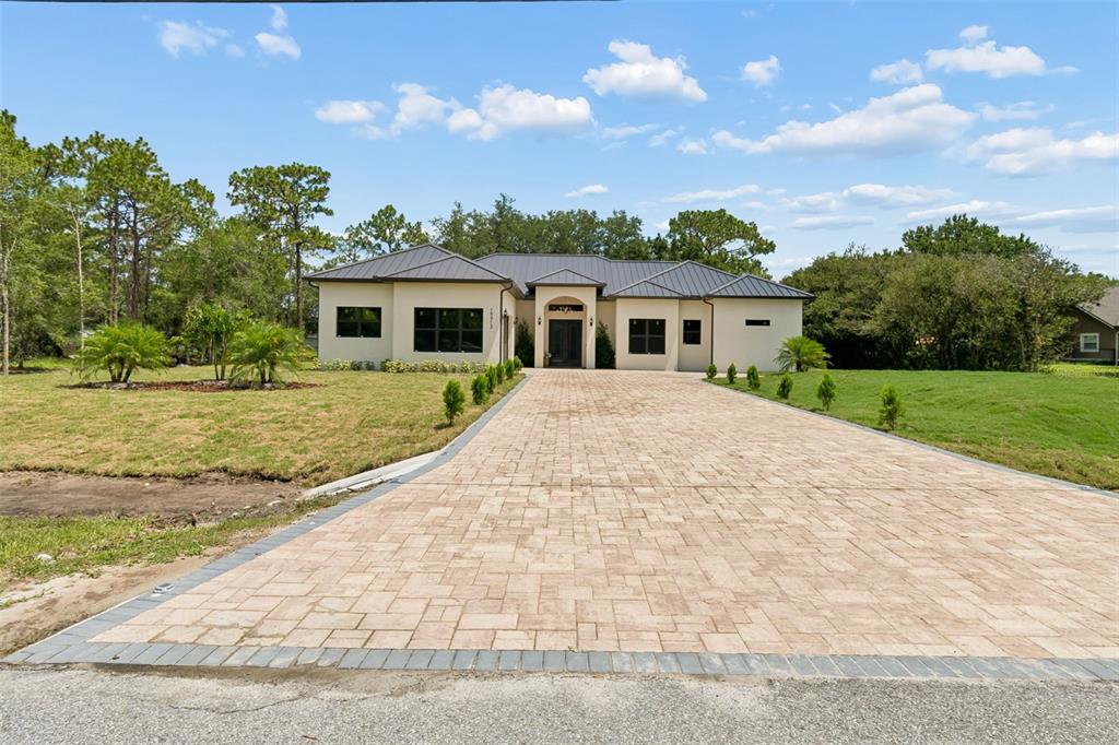 A single-story house with a paved driveway, dark metal roof, and light-colored stucco exterior — 19913 MOORGATE STREET, ORLANDO, FL