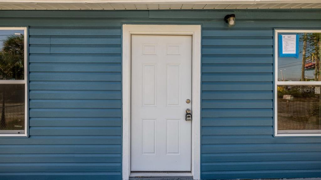A white front door is centered between two windows on a blue horizontal-sided exterior wall — 7508 CAROLYN AVENUE, ORLANDO, FL