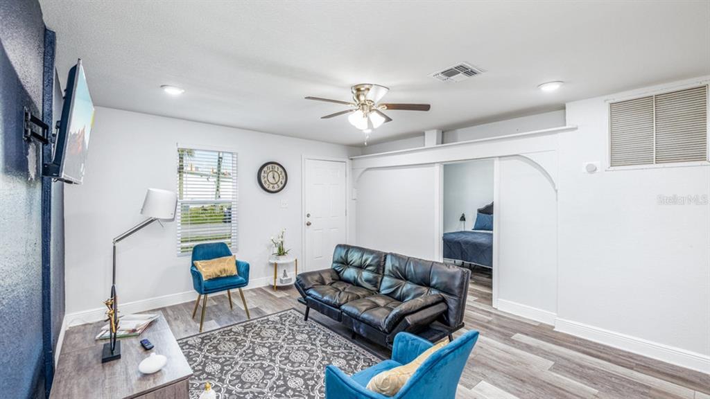 A living room features a black sofa, two blue chairs, and an adjacent bedroom doorway — 7508 CAROLYN AVENUE, ORLANDO, FL