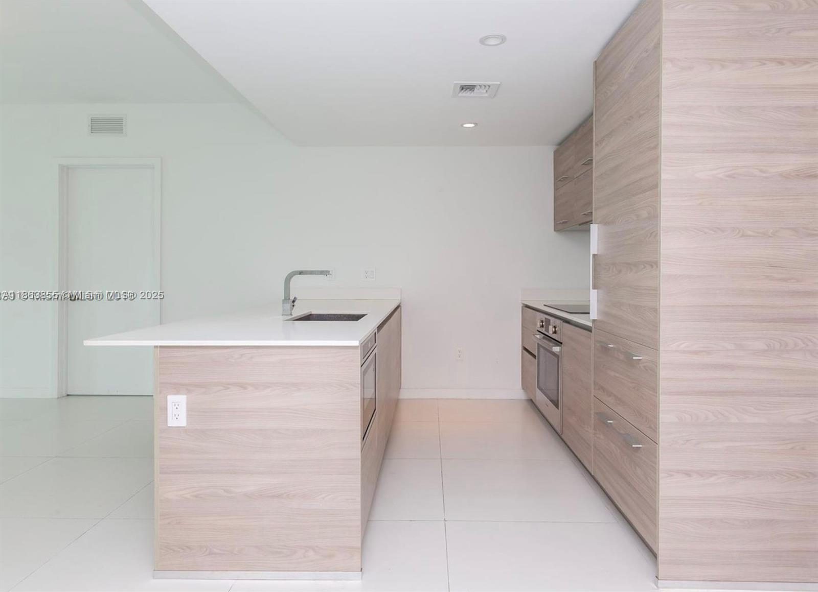 A modern kitchen features light wood-grain cabinetry, a white island with a sink, and tile flooring — 1300 S Miami Ave # 1602, Miami FL 33130, MIAMI, FL