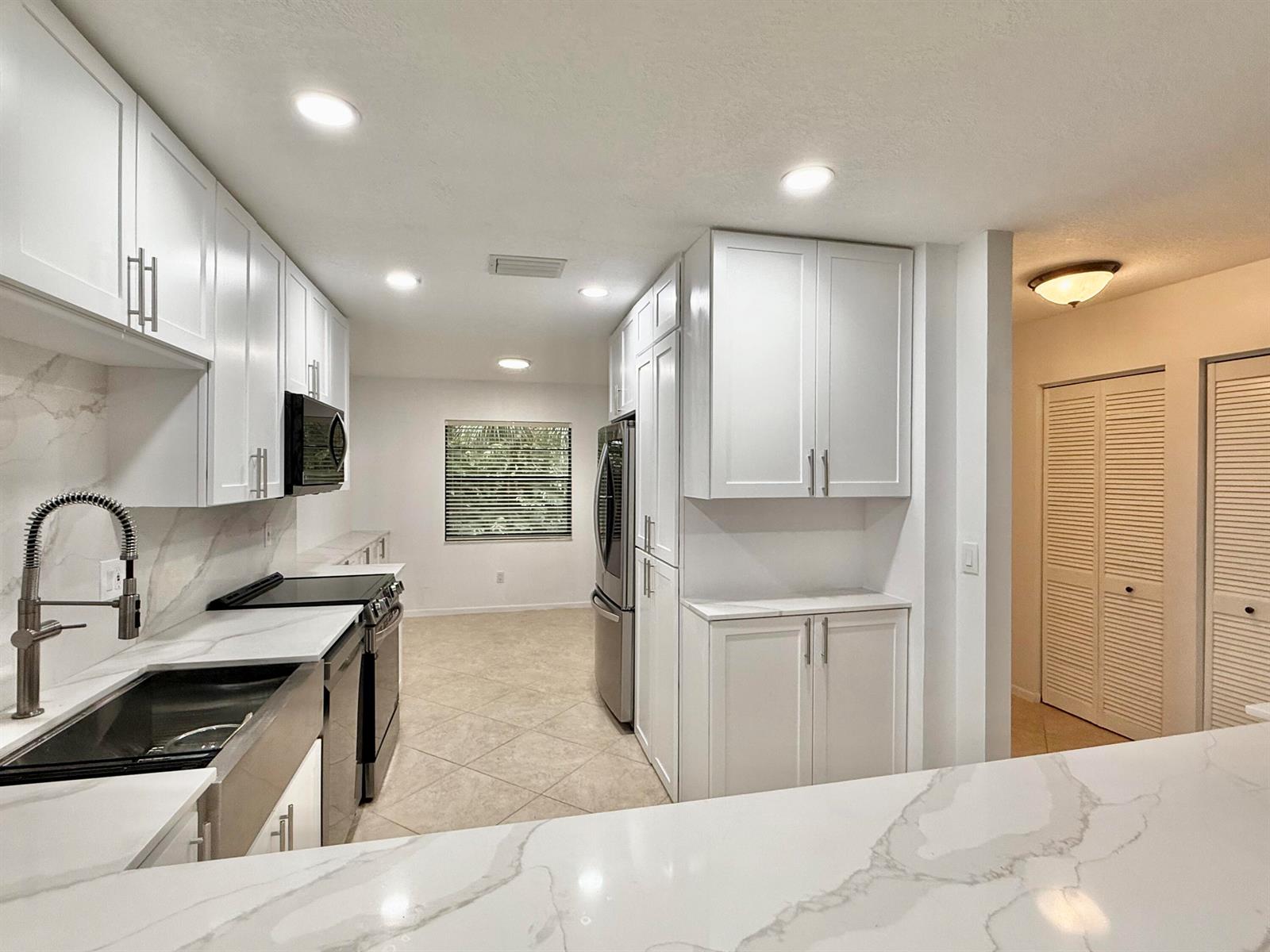 A modern kitchen features white cabinets, marble-look countertops, stainless steel appliances, and tile flooring — 22 Westgate Lane # 22h, Boynton Beach FL 33436, BOYNTON BEACH, FL