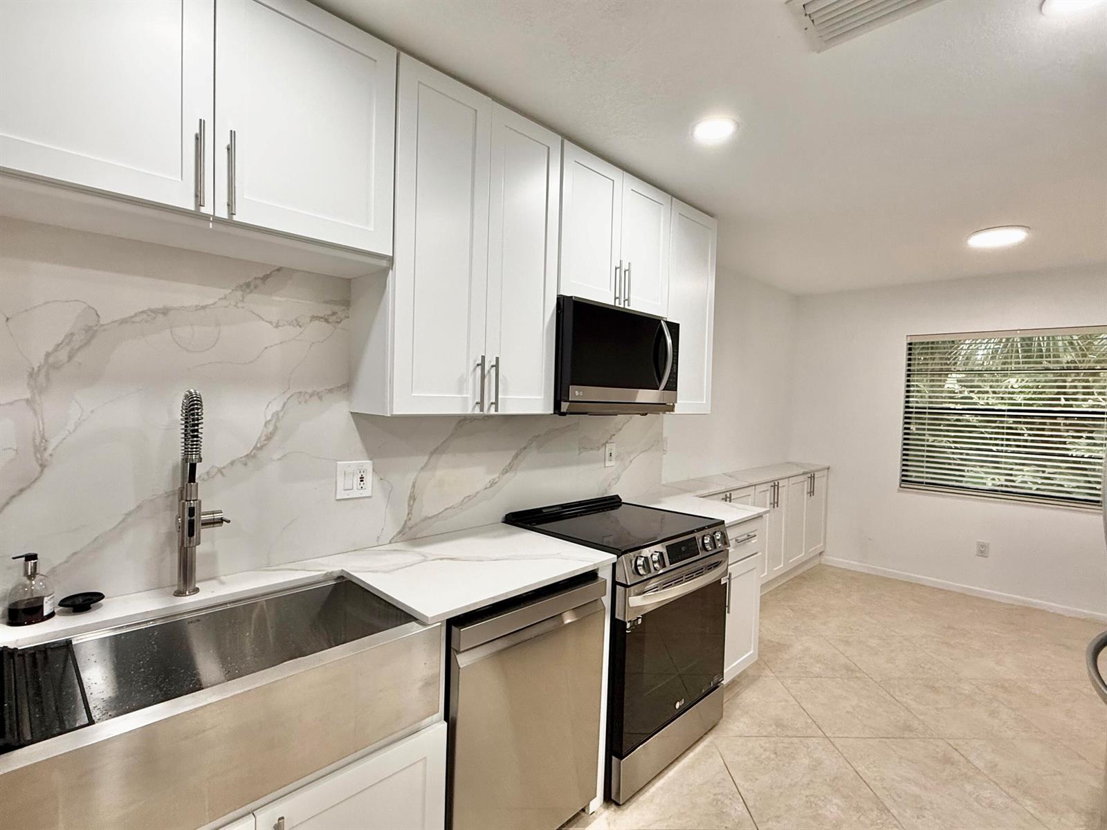 A kitchen features white cabinets, stainless steel appliances, a farmhouse sink, and marble-patterned countertops — 22 Westgate Lane # 22h, Boynton Beach FL 33436, BOYNTON BEACH, FL