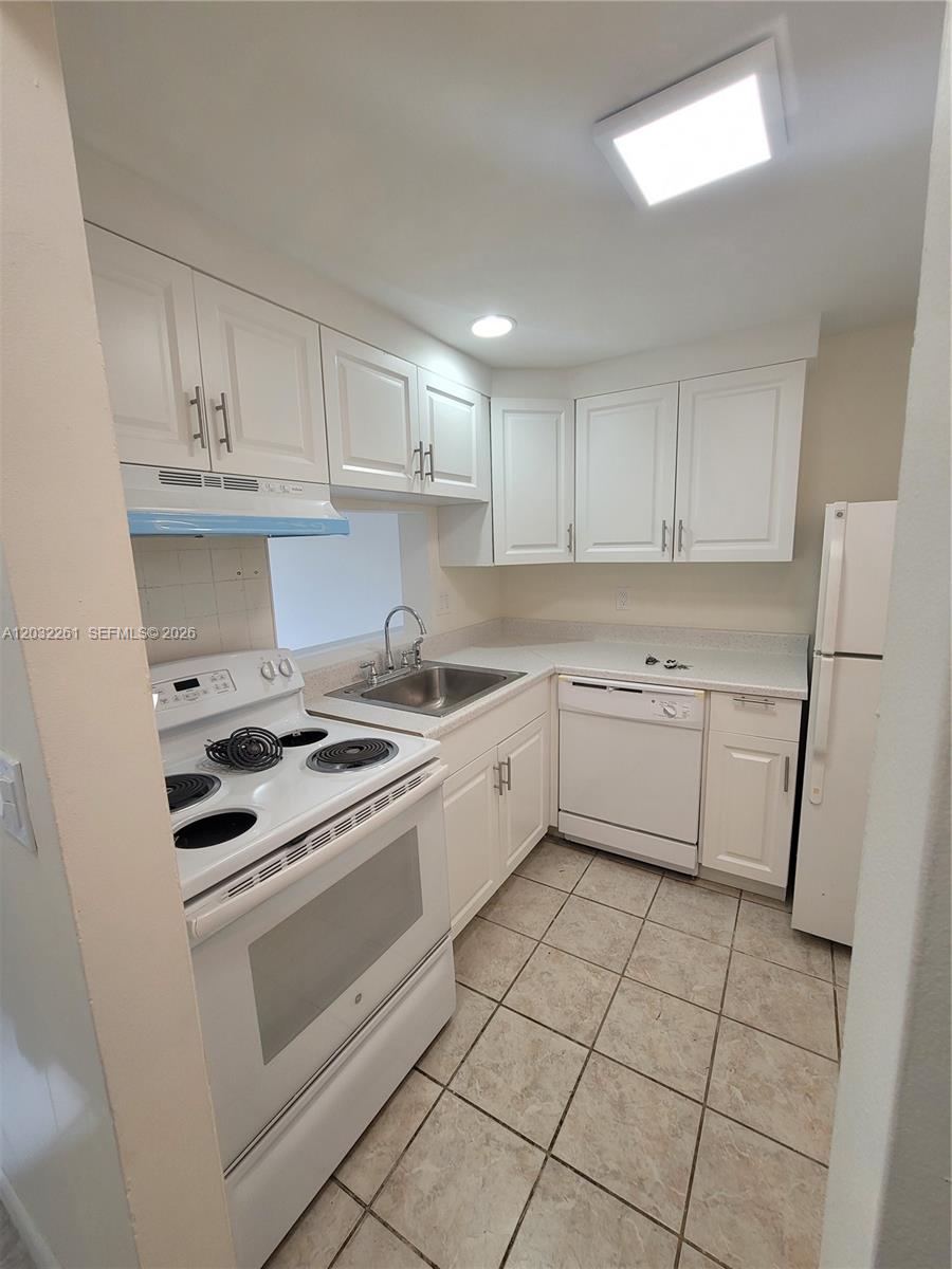 A small kitchen features white cabinets, white appliances, and light-colored tile flooring — 2800 NW 56th Ave # E401, Lauderhill FL 33313, LAUDERHILL, FL