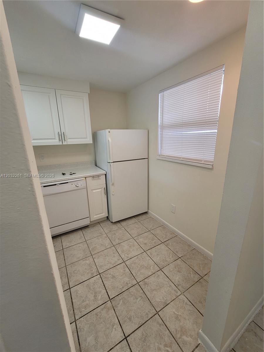 A small kitchen features white cabinets, a dishwasher, a refrigerator, and tiled flooring — 2800 NW 56th Ave # E401, Lauderhill FL 33313, LAUDERHILL, FL