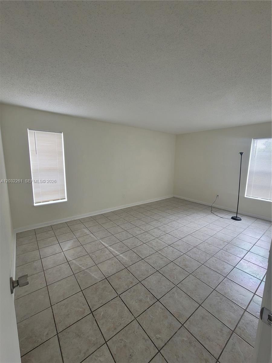 An empty room features light-colored tile flooring, white walls, two windows with blinds, and a lamp — 2800 NW 56th Ave # E401, Lauderhill FL 33313, LAUDERHILL, FL