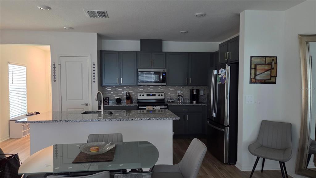 A kitchen features dark gray cabinets, granite countertops, stainless steel appliances, and a dining area — 728 STONEY POINT CIRCLE, DAVENPORT, FL