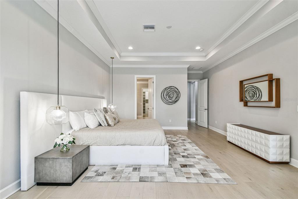 A modern bedroom features a large white upholstered bed, pendant lighting, and light wood flooring — 4054 ROCKY SHORES DRIVE, TAMPA, FL