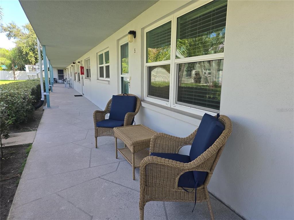 A covered outdoor walkway features two wicker chairs with blue cushions and a small table — 5267 81ST STREET N UNIT 5, ST PETERSBURG, FL