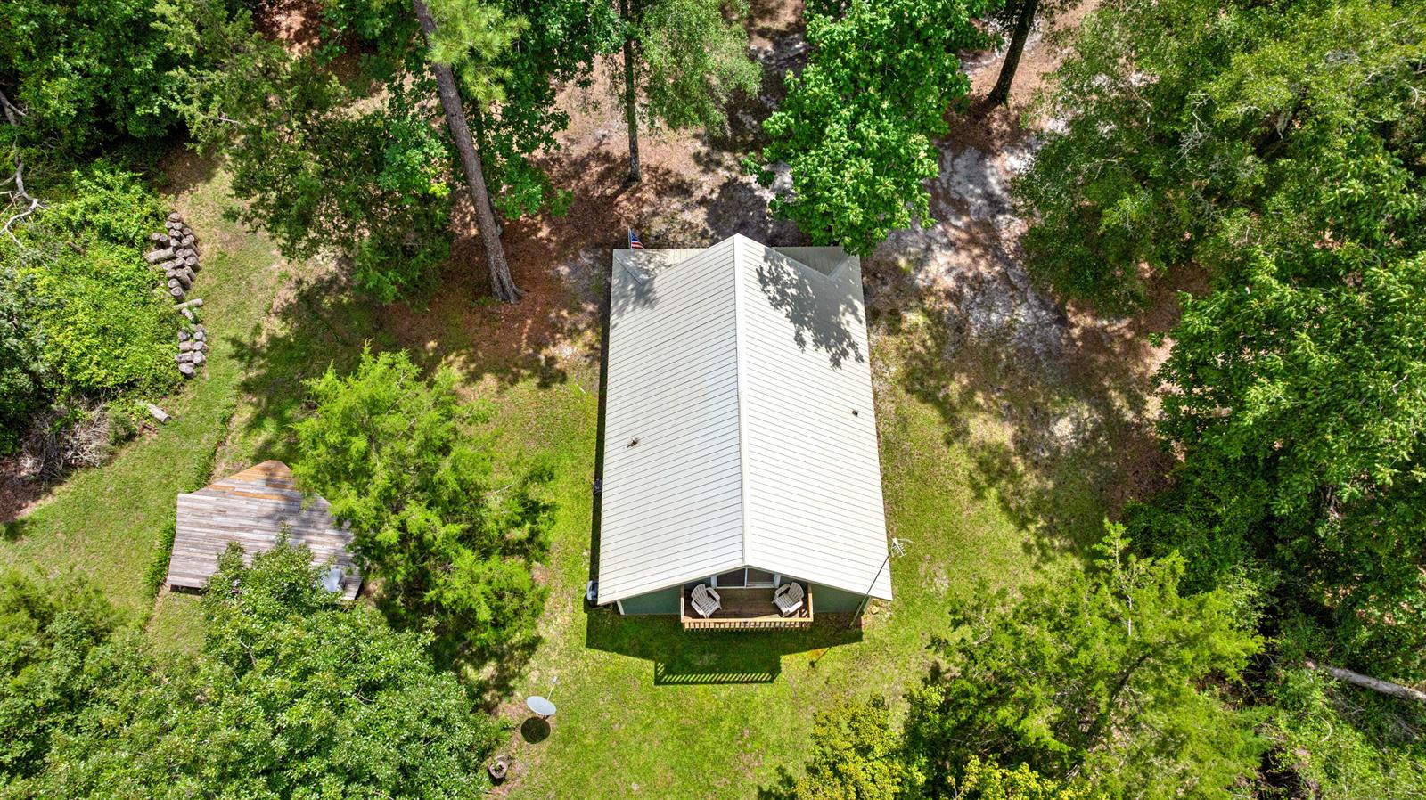 An aerial view shows a cabin with a metal roof, a deck, and surrounding trees — 694 SW Quarter Lane, FL 32038, FL