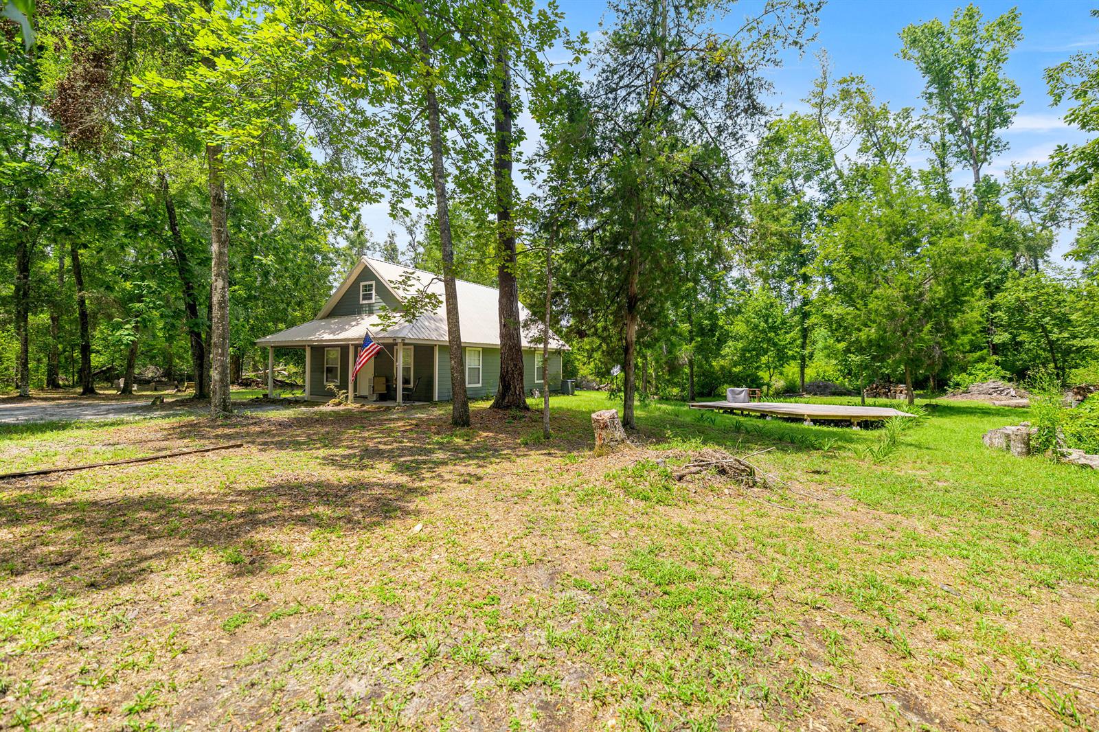 A green house with a metal roof and a front porch sits in a wooded yard — 694 SW Quarter Lane, FL 32038, FL