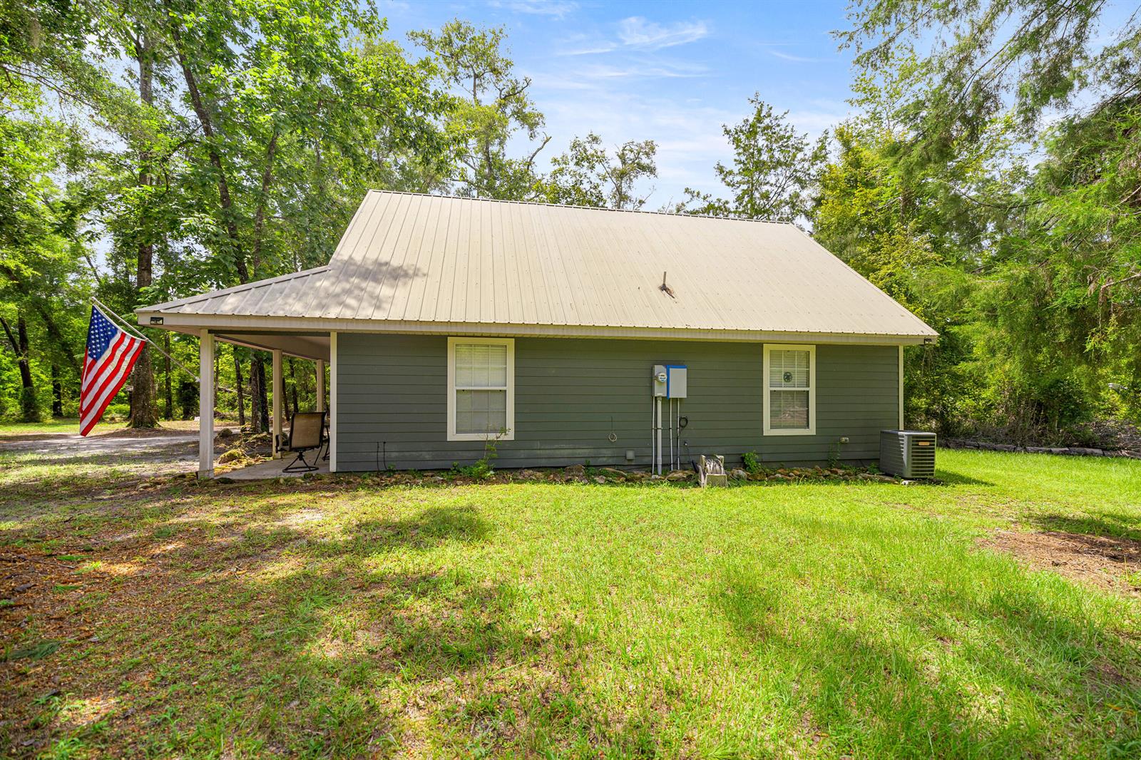 A gray house with a metal roof and a covered porch stands in a wooded yard — 694 SW Quarter Lane, FL 32038, FL
