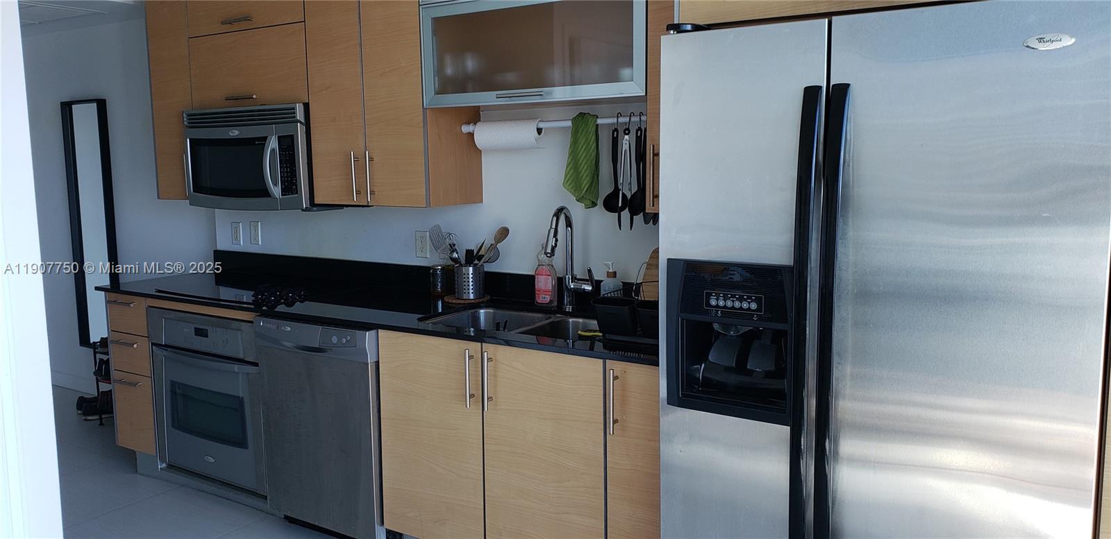 A kitchen features light wood cabinets, black countertops, and stainless steel appliances — 60 SW 13th St # 1621, Miami FL 33130, MIAMI, FL