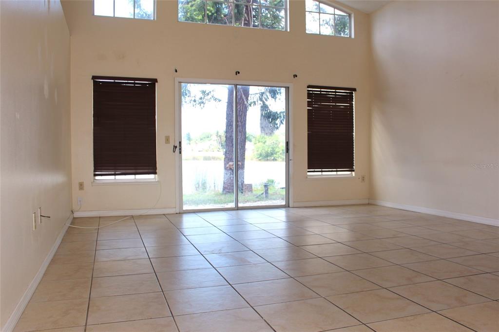 An empty room features tile flooring, large windows, and sliding glass doors overlooking a lake — 3036 DELLCREST PLACE, LAKE MARY, FL