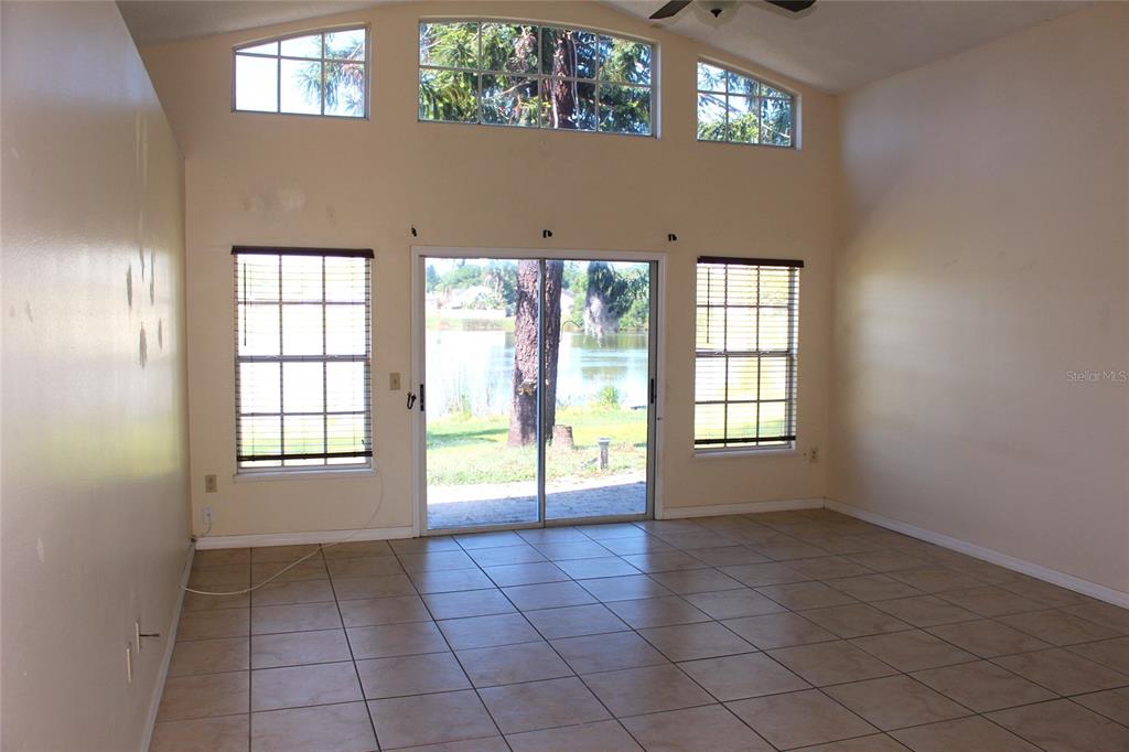 An empty living room features tile flooring, vaulted ceilings, and sliding doors overlooking a lake — 3036 DELLCREST PLACE, LAKE MARY, FL
