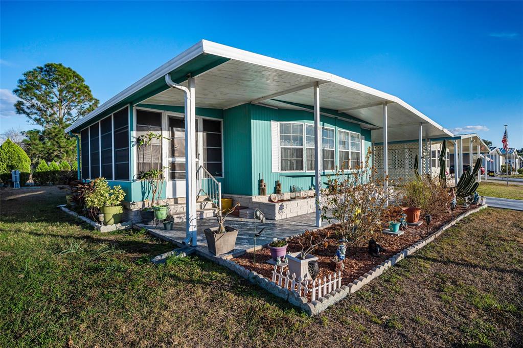 A teal mobile home features a screened-in porch, a covered carport, and a landscaped yard — 3318 CARNATION LANE, ZEPHYRHILLS, FL