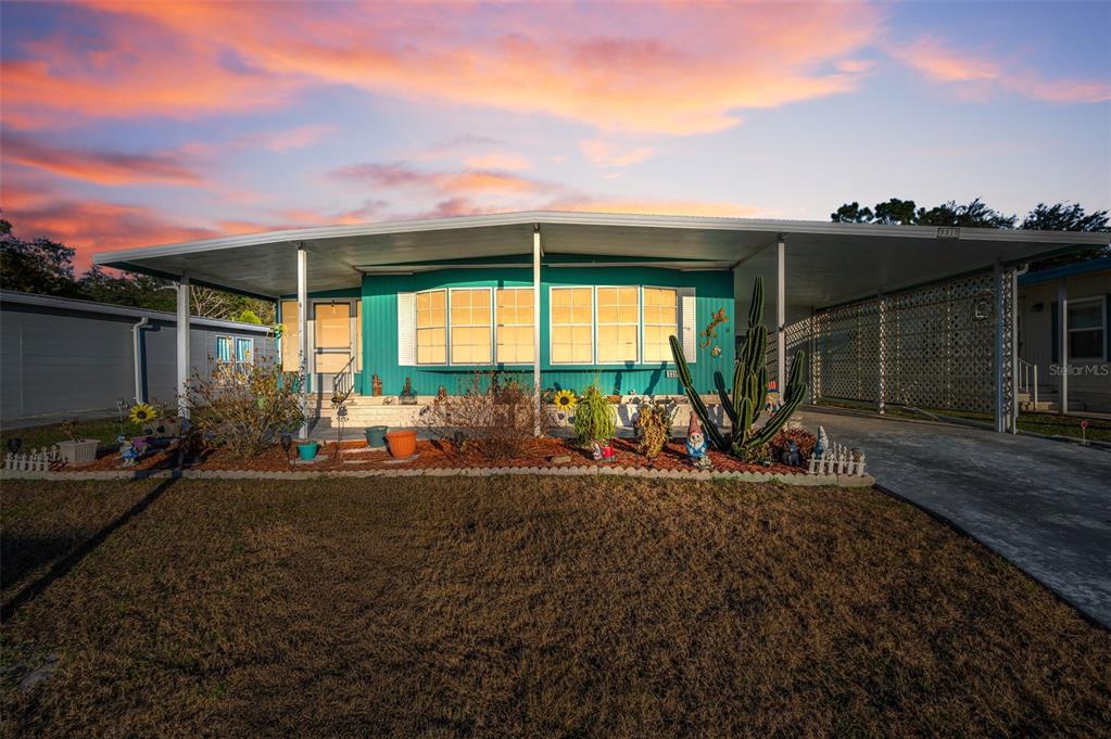 A teal mobile home with a large carport and a front lawn at sunset — 3318 CARNATION LANE, ZEPHYRHILLS, FL