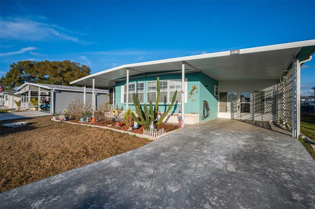 A teal mobile home features a large cactus, a concrete driveway, and a covered carport — 3318 CARNATION LANE, ZEPHYRHILLS, FL