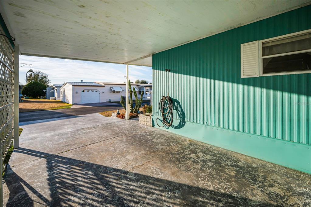 A covered concrete carport sits beside a teal-sided mobile home with a white window shutter — 3318 CARNATION LANE, ZEPHYRHILLS, FL