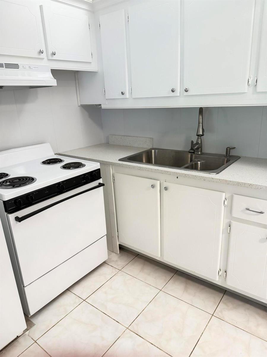 A kitchen features white cabinets, a white electric stove, and a stainless steel double sink — 179 Windsor H, West Palm Beach FL 33417, WEST PALM BEACH, FL