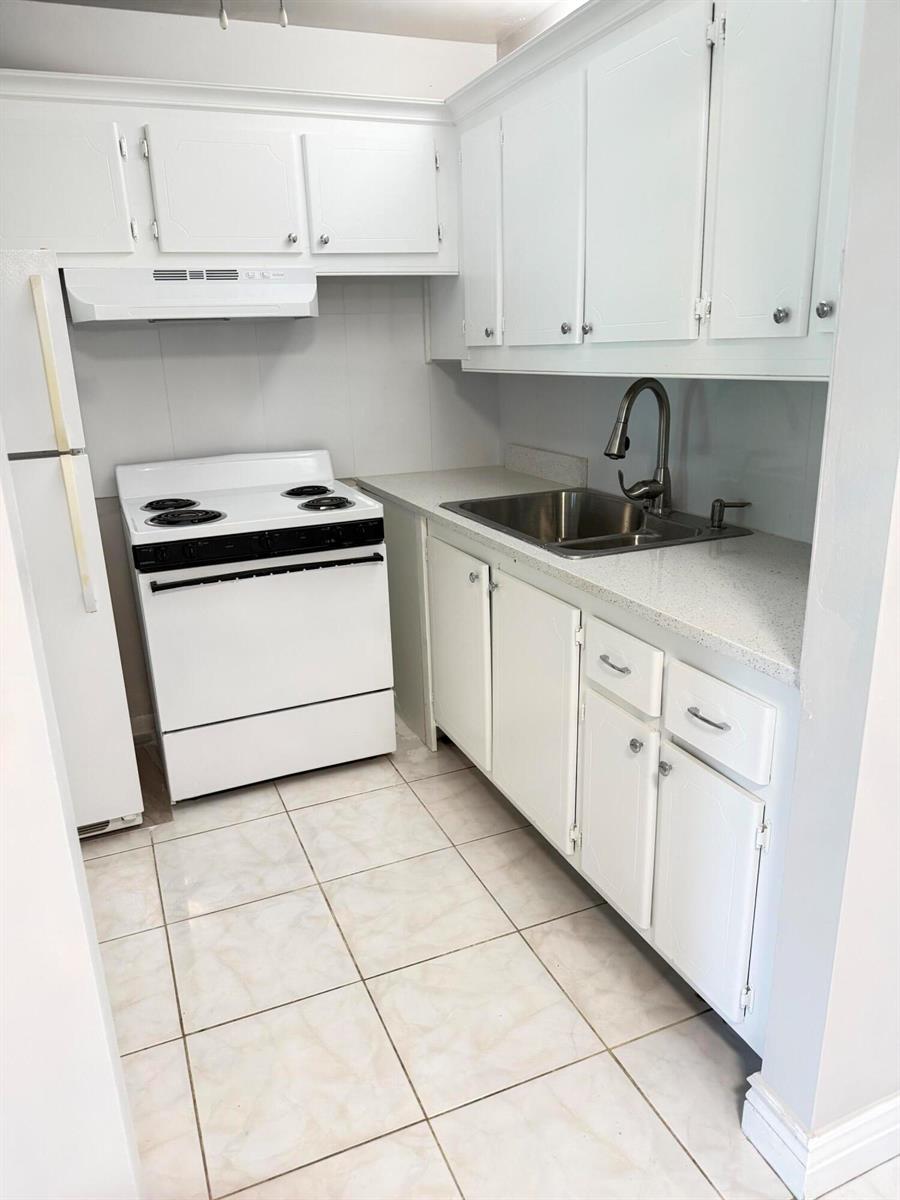A small kitchen features white cabinets, a white stove, a stainless steel sink, and tile flooring — 179 Windsor H, West Palm Beach FL 33417, WEST PALM BEACH, FL