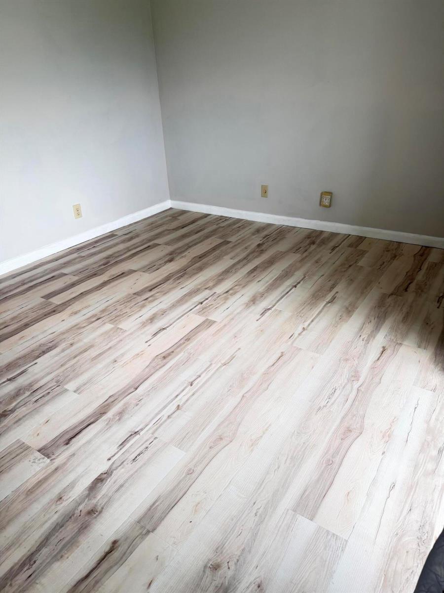 An empty room features light-toned wood-look flooring and plain gray walls with baseboards — 179 Windsor H, West Palm Beach FL 33417, WEST PALM BEACH, FL