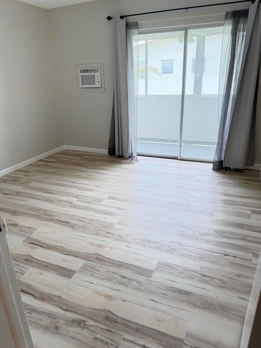 An empty room features light wood-look flooring, a wall-mounted air conditioner, and sliding glass doors — 179 Windsor H, West Palm Beach FL 33417, WEST PALM BEACH, FL