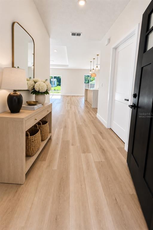 A bright entryway features light wood flooring, a console table, and a view toward the kitchen — 2860 SE 146TH PLACE, SUMMERFIELD, FL