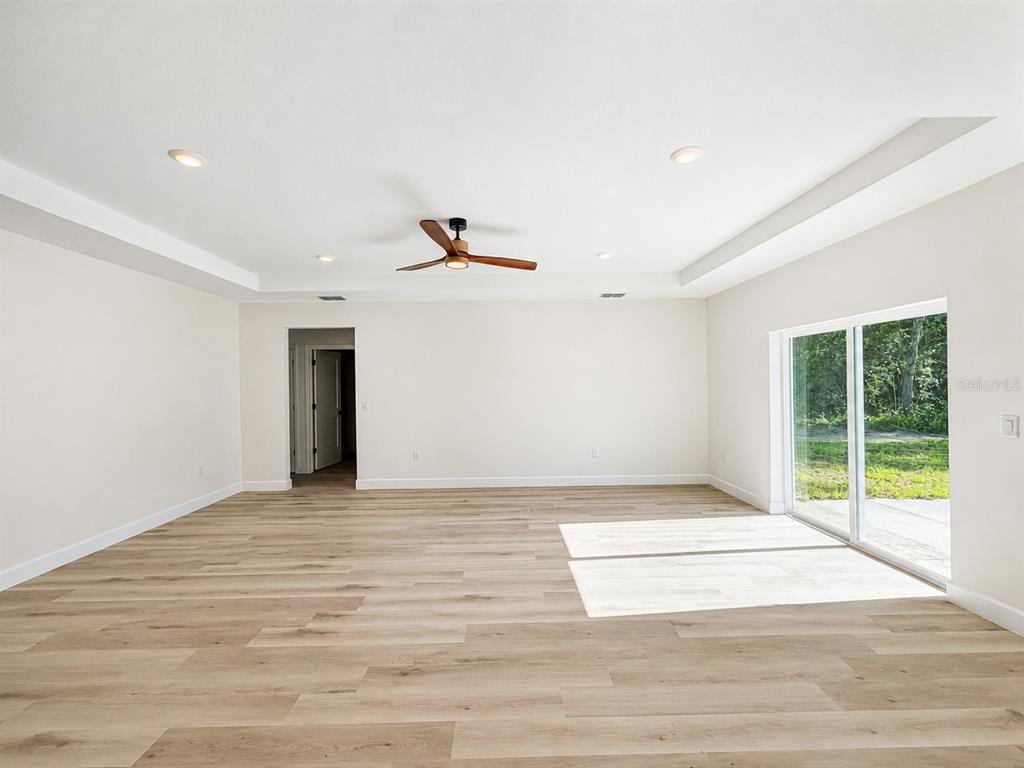 A spacious room with light wood flooring, a tray ceiling, a ceiling fan, and sliding doors — 2860 SE 146TH PLACE, SUMMERFIELD, FL
